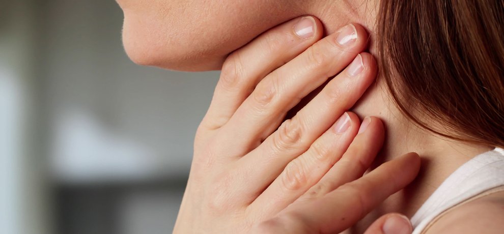 Mujer serena con una mano en la garganta sobre fondo beige neutro, luz natural suave