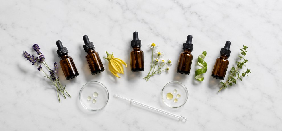 Cinco frascos ambar de Aceites Esenciales con lavanda, ylang ylang, manzanilla, bergamota y mejorana sobre superficie blanca